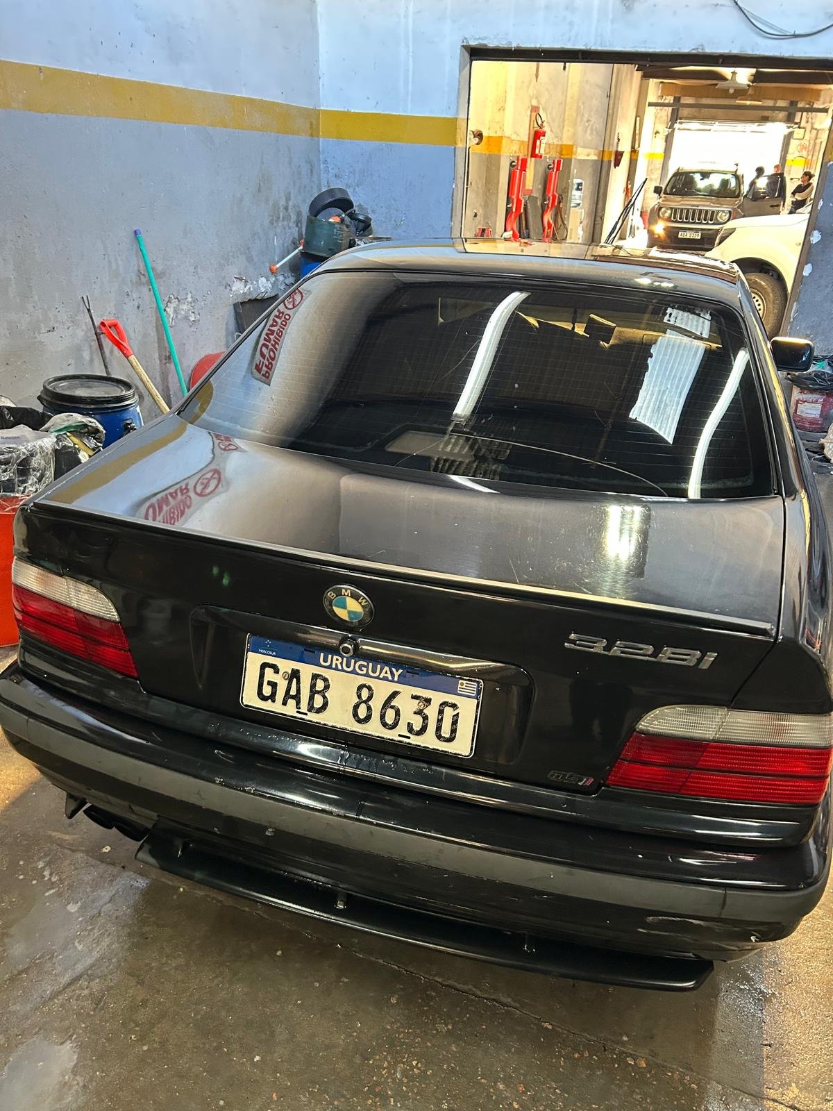 BMW 328i negro de atrás, con matrícula uruguaya, dentro del taller