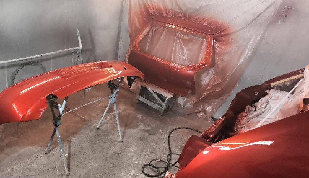Paragolpes, puerta y capot recién pintados en color cobre metalizado, en la cabina de pintura